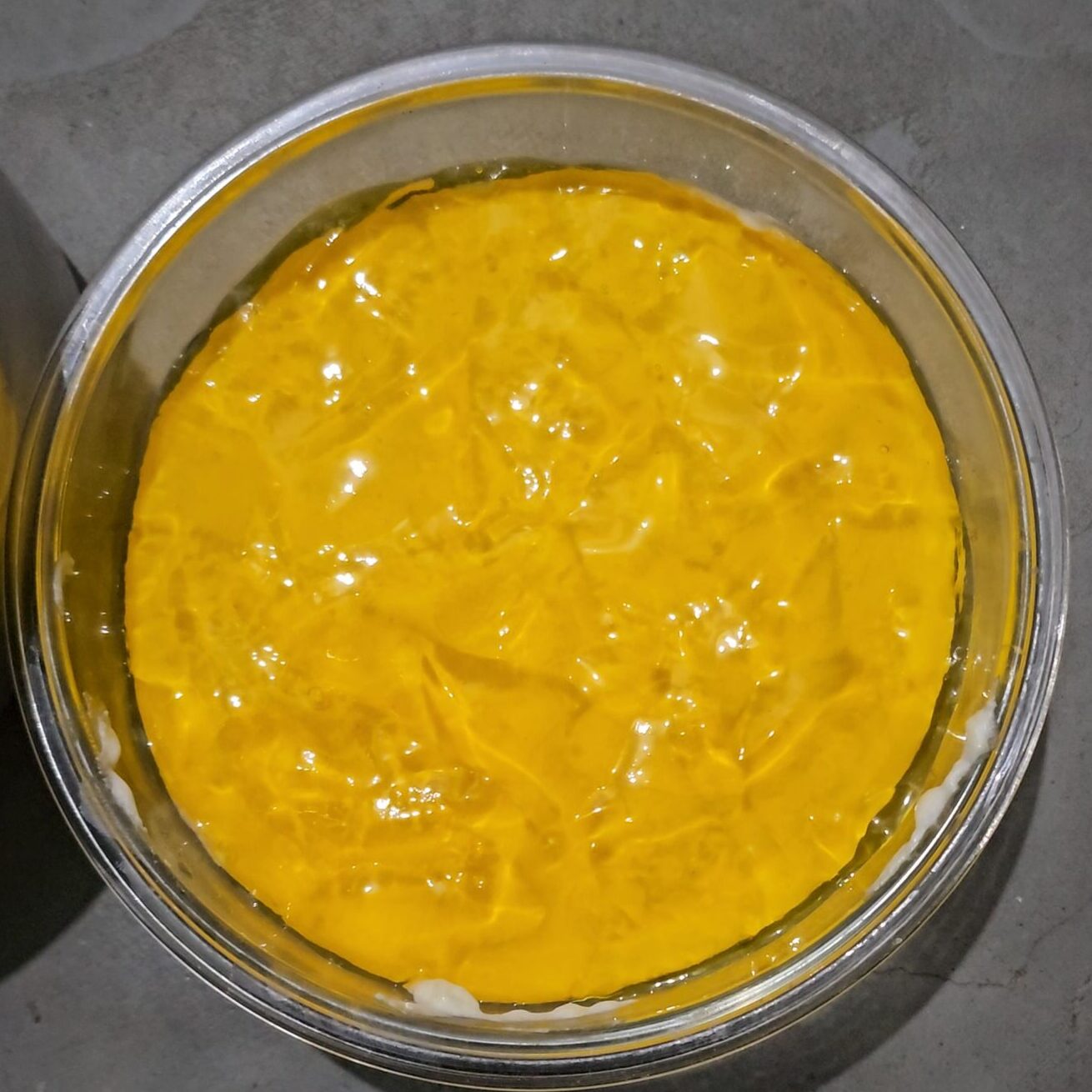 Mango jelly layer being poured on cheesecake